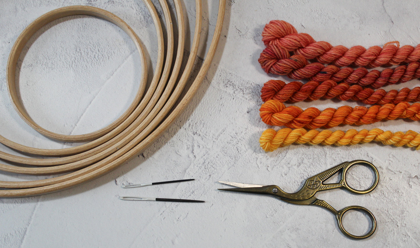 A selection of wooden rings, stock shaped scissors, needles and red and orange yarns.