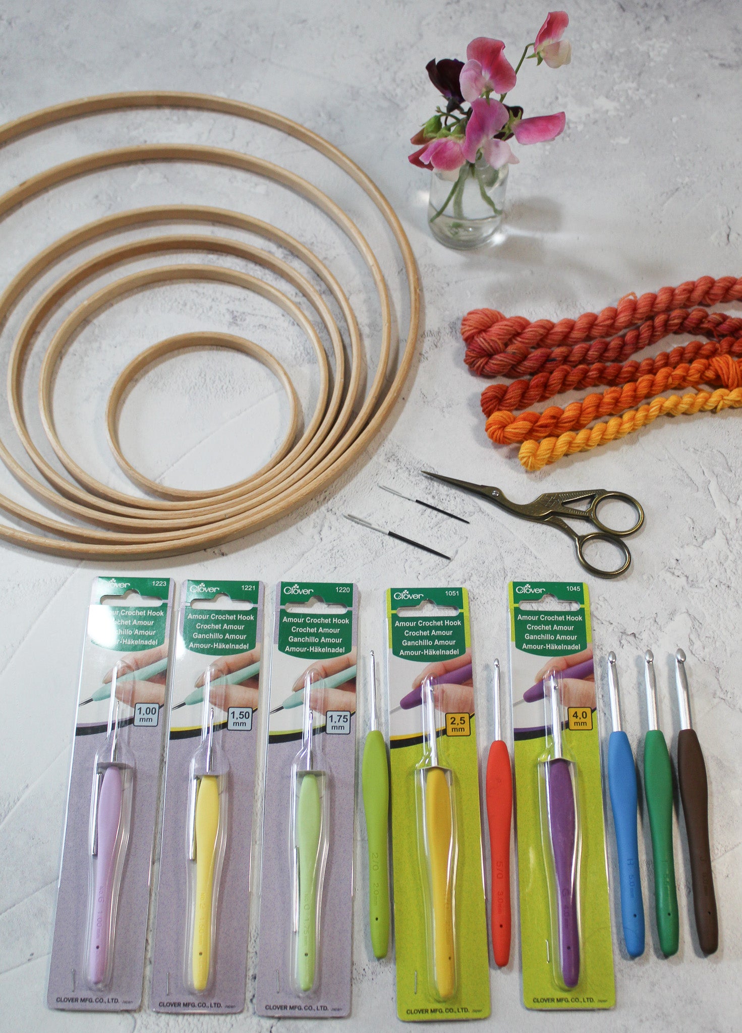 Clover Armor crochet hooks, wooden rings for crochet, macrame or other craft, needles, scissors and yarns and a small vase of sweetpeas