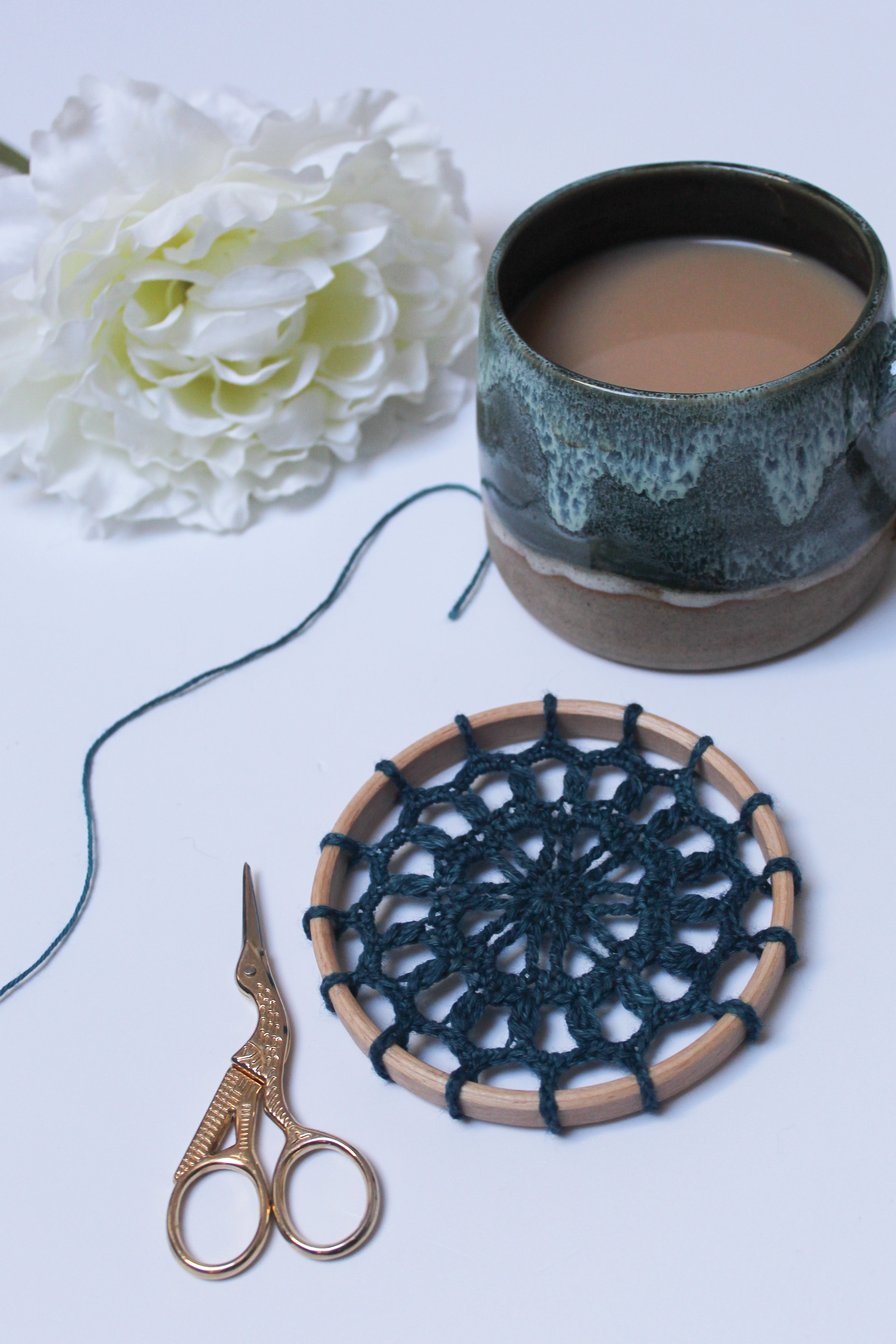 Crocheted hoop with blue yarn, scissors, and a mug on a light surface.