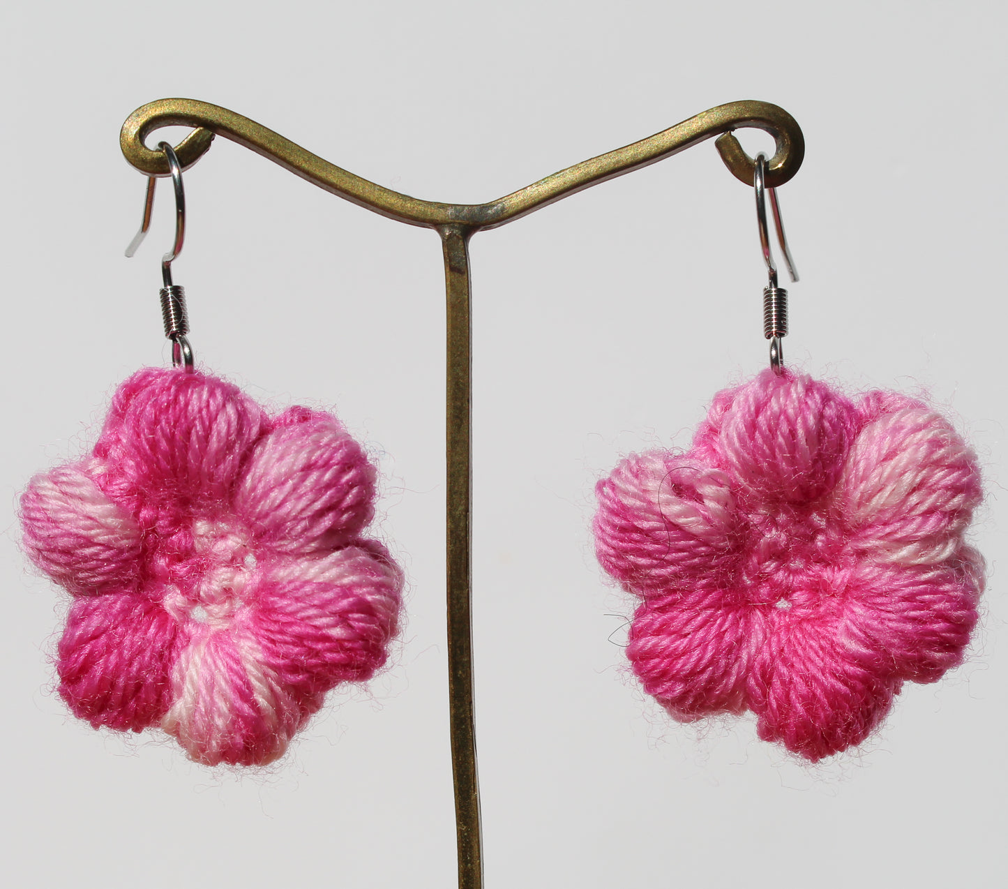 Pink flower-shaped earrings on a stand against a light background