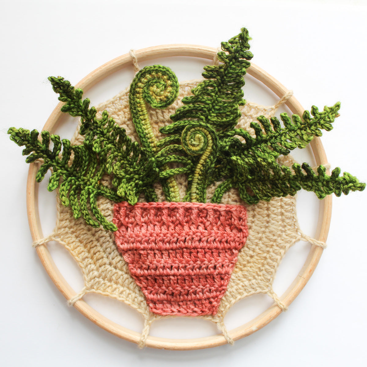 A crochet mandala featuring green fern fronds and spiral fronds rising from a terracotta planter.