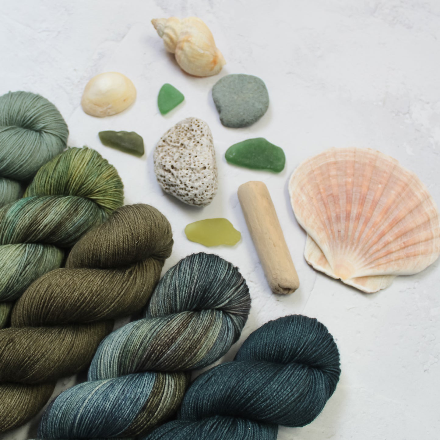 Selection of yanrs to make the Rough Seas crochet mandala, shades of blues and greens, styled with shells and seaglass, stones and driftwood