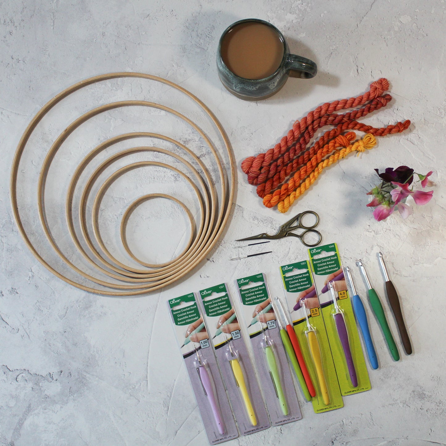 Clover Armor crochet hooks, wooden rings for crochet, macrame or other craft, needles, scissors and yarns and a small vase of sweetpeas